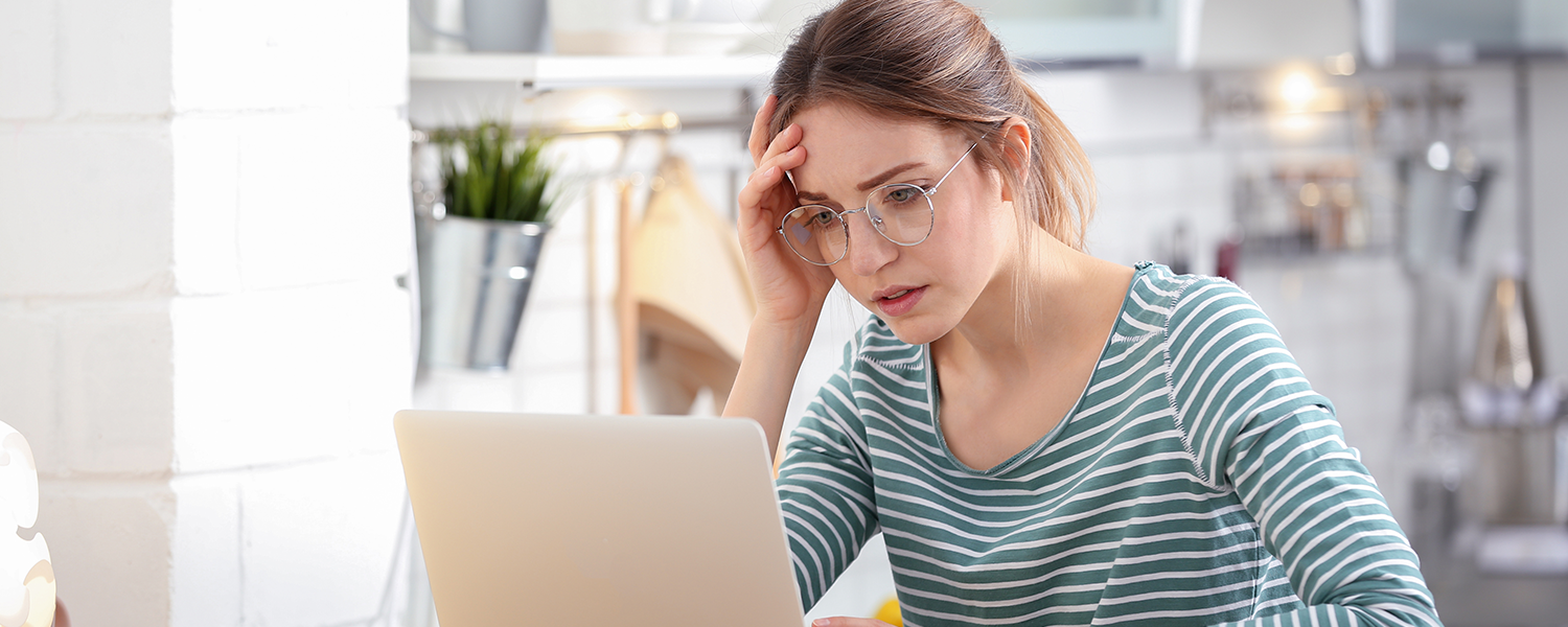 A woman using a laptop at a kitchen table with a smartphone nearby.